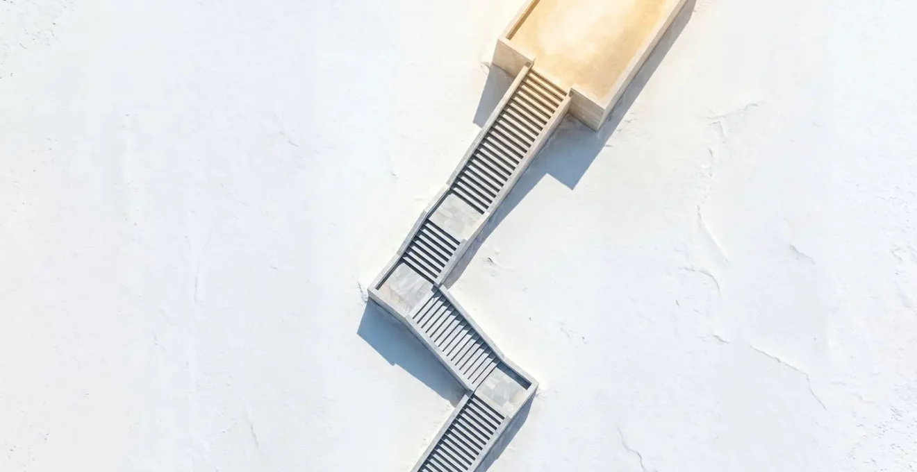 Vue aérienne d'un escalier monumental en pierre claire serpentant à travers un désert de sel blanc vers un plateau lumineux, symbolisant le parcours progressif de migration cloud